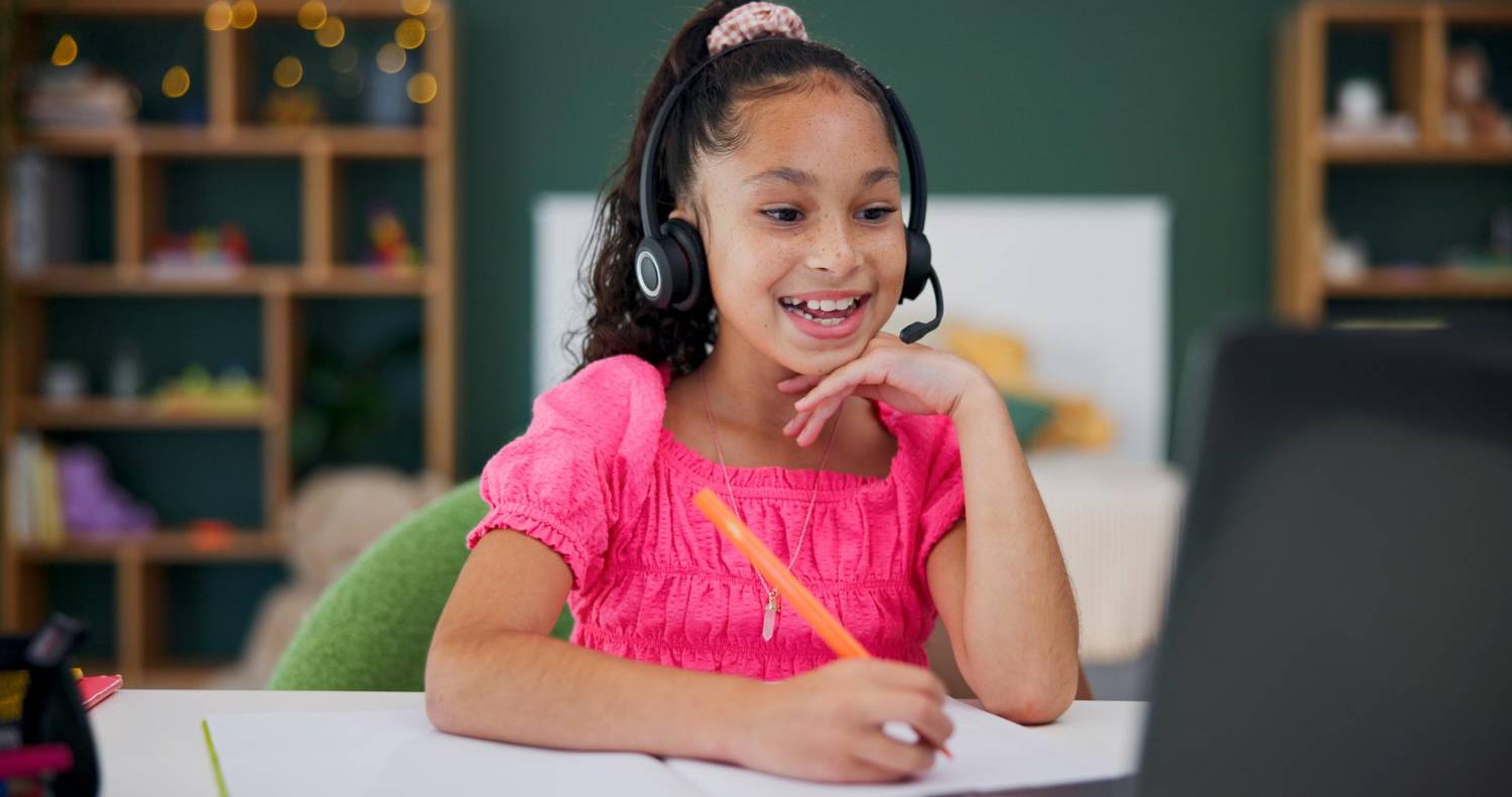 Online elementary school student learning from Wellspring Young girl with headphones smiling during online elementary school class